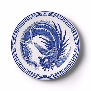 May include: A white ceramic plate with a blue phoenix design. The phoenix is depicted with detailed feathers and a long tail. The plate has a blue geometric border.