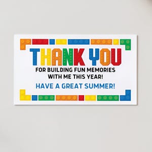Könnte beinhalten: Eine weiße rechteckige Karte mit den Worten "THANK YOU" in bunten Blockbuchstaben. Die Karte sagt auch "FOR BUILDING FUN MEMORIES WITH ME THIS YEAR! HAVE A GREAT SUMMER!". Die Karte ist mit bunten Blockdesigns verziert.