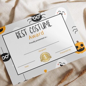 May include: A Halloween-themed award certificate with the text "BEST COSTUME Award" in black. The certificate has a white background with a gray border and is decorated with cartoon spiders, pumpkins, and ghosts.