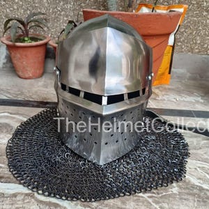 May include: A polished steel helmet with a riveted chainmail aventail. The helmet has a rectangular face opening and small ventilation holes. The text "TheHelmetCollection" is visible on the helmet.
