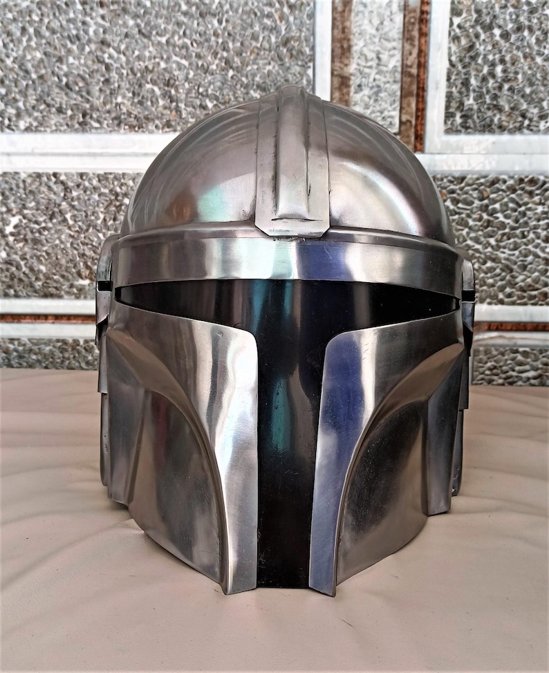 May include: A metallic silver helmet with a black visor. The helmet has a rounded top with a central ridge and angular features around the face and sides. The surface reflects light, creating highlights and shadows.