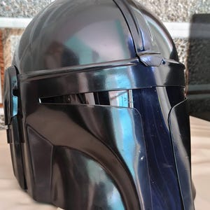 May include: A glossy black helmet with a distinctive visor and angular design. The helmet has a smooth, reflective surface and appears to be made of a durable material. The overall shape suggests a futuristic or sci-fi theme.
