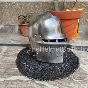 May include: A polished steel helmet with a visor and ventilation holes, resting on a chainmail coif. The helmet has a rounded top and a rectangular visor. The text "TheHelmetCollection" is visible on the image.