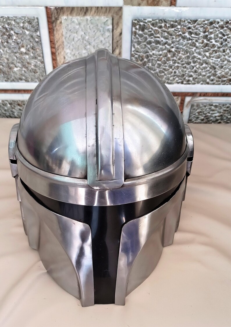 May include: A metallic silver helmet with a black visor. The helmet has a rounded top with vertical ridges and a curved front. The design is reminiscent of a space-themed character.