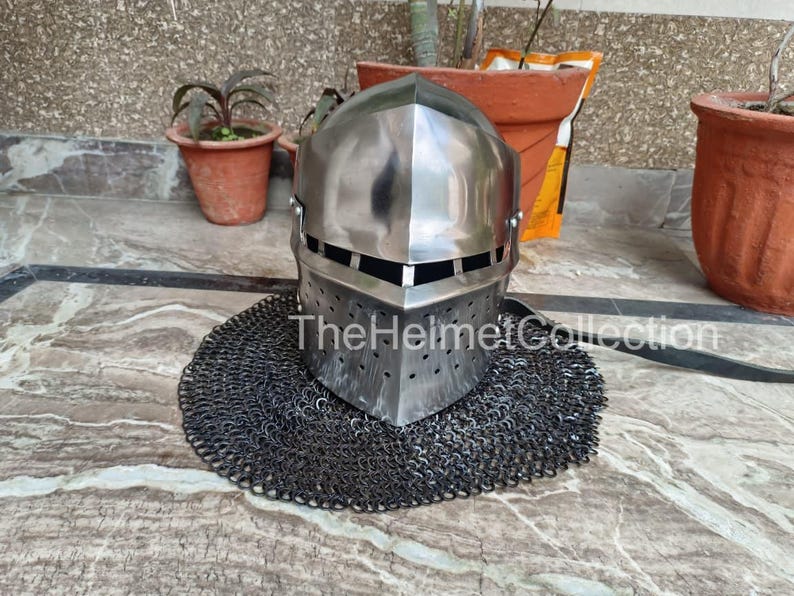 May include: A polished steel helmet with a riveted chainmail aventail. The helmet has a rectangular face opening and small ventilation holes. The text "TheHelmetCollection" is visible on the helmet.