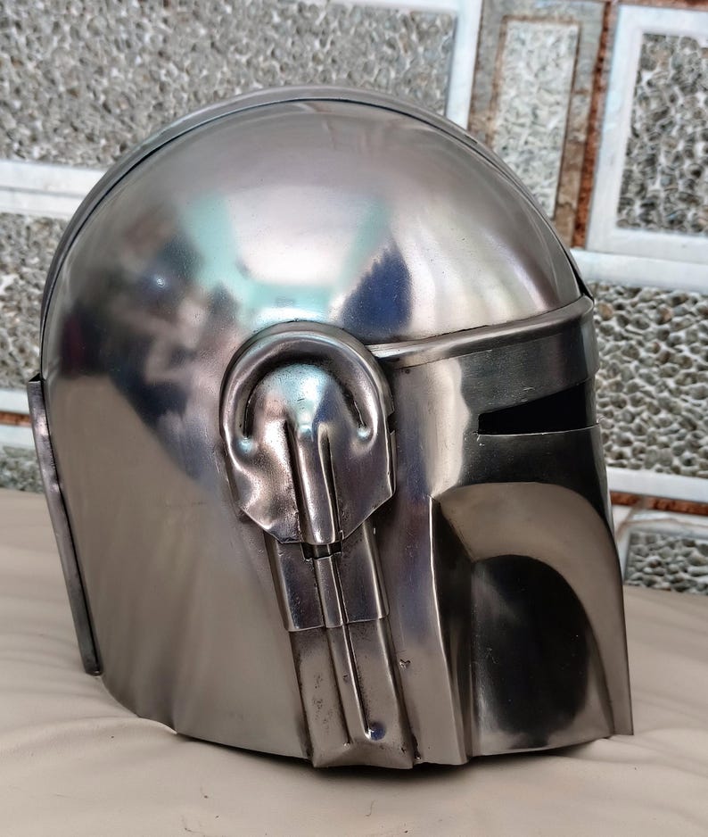 May include: A metallic silver helmet with a visor and distinctive ear-like protrusions. The helmet has a smooth, reflective surface, suggesting a polished metal finish. The design is reminiscent of a science fiction or fantasy theme.