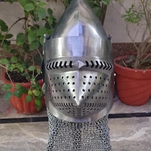 Peut inclure: Un casque m&eacute;di&eacute;val en acier poli avec un sommet pointu et une visi&egrave;re avec de petits trous et fentes pour la vision et la ventilation. Le casque est fix&eacute; &agrave; une protection de cou en cotte de mailles. Le casque est expos&eacute; sur un support noir.