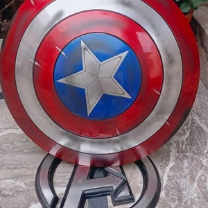 May include: A Captain America shield prop, featuring a red, white, and blue color scheme. The shield has a circular design with a central blue circle and a white star. The shield is approximately 24 inches in diameter.