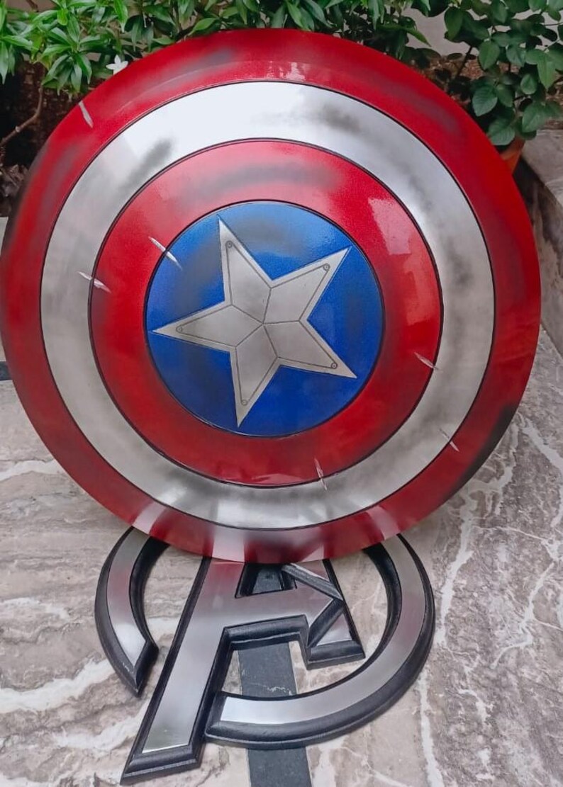 May include: A Captain America shield prop, featuring a red, white, and blue color scheme. The shield has a circular design with a central blue circle and a white star. The shield is approximately 24 inches in diameter.