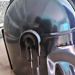 May include: A dark gray helmet with a glossy finish. The helmet has a rounded top and a visor area. A curved, rectangular detail is on the side. The helmet appears to be made of a hard, durable material.