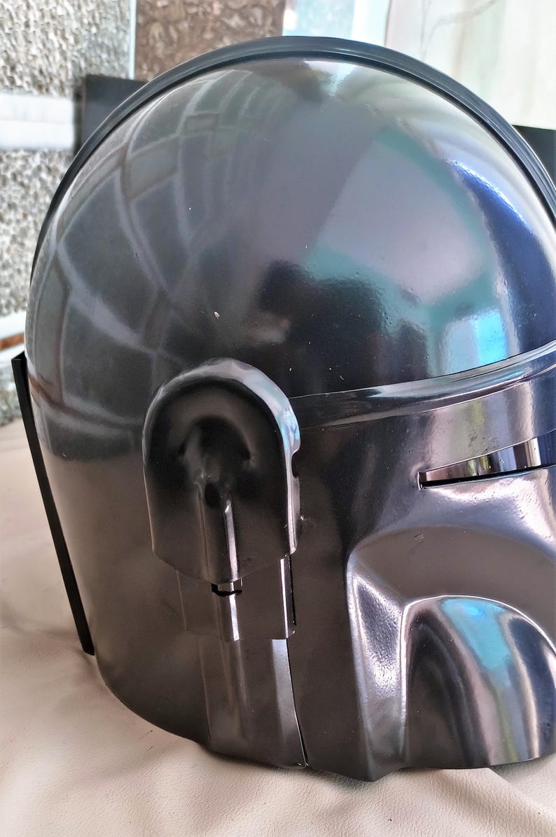 May include: A dark gray helmet with a glossy finish. The helmet has a rounded top and a visor area. A curved, rectangular detail is on the side. The helmet appears to be made of a hard, durable material.