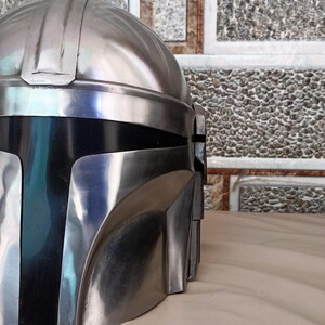 May include: A metallic silver and black helmet with a distinctive design. The helmet features a rounded top with vertical ridges and a visor area. The lower section is black, contrasting with the silver upper portion. The helmet is likely a prop or costume piece.