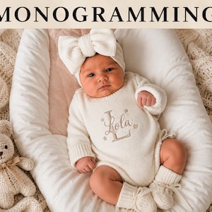 May include: A cream-colored long-sleeve knit bodysuit featuring the embroidered name Lola with a large letter L and small star accents. The outfit includes a matching ribbed knit headband with a large bow and cream-colored knit booties.
