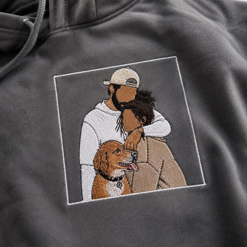 May include: A charcoal gray hooded sweatshirt featuring a square embroidered patch. The embroidery depicts two figures embracing, one wearing a white long-sleeve shirt and a beige baseball cap, the other in a tan jacket, alongside a golden-brown dog.
