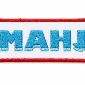 May include: A rectangular embroidered patch with a white background and a thick red border. The letters MAHJ are stitched in bright blue with a lighter blue shadow effect along the bottom edge of each letter, creating a three-dimensional appearance.