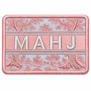 May include: A rectangular embroidered patch featuring a light blue background with pink cherry blossom trees on the top and bottom. The centre contains the white capital letters MAHJ set against a pink horizontal band with a decorative border.