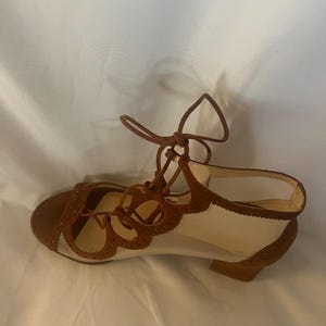 Op de afbeelding: Bruine en cr&egrave;mekleurige vetersandalen. De sandalen hebben een bruine su&egrave;de neus en hiel, met een cr&egrave;mekleurig mesh bovenwerk. Het ontwerp omvat decoratieve uitgesneden details en een kleine hak. De veters zijn bruin.
