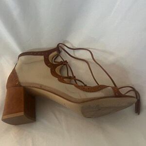 Op de afbeelding: Een bruin en beige sandalen met hak en een vetersluiting. De schoen heeft een bruine su&egrave;de blokhak, een beige mesh bovenwerk en bruine leren afwerking met een geschulpte rand. De veters zijn bruin.