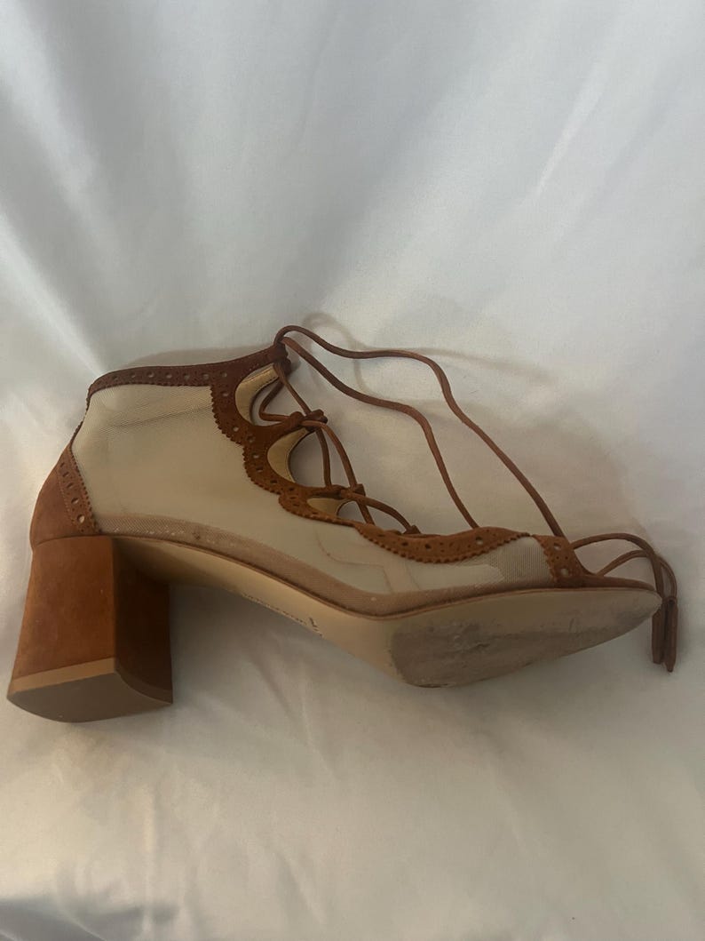 Op de afbeelding: Een bruin en beige sandalen met hak en een vetersluiting. De schoen heeft een bruine su&egrave;de blokhak, een beige mesh bovenwerk en bruine leren afwerking met een geschulpte rand. De veters zijn bruin.