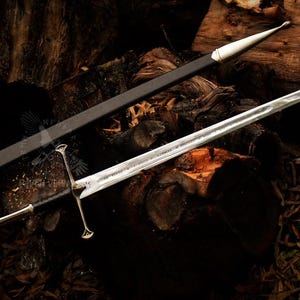 May include: A silver sword with a double-edged blade and a decorative hilt, resting on a wooden surface. The sword is accompanied by a black sheath with white accents. The overall design suggests a medieval or fantasy theme.