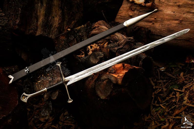 May include: A silver sword with a double-edged blade and a decorative hilt, resting on a wooden surface. The sword is accompanied by a black sheath with white accents. The overall design suggests a medieval or fantasy theme.