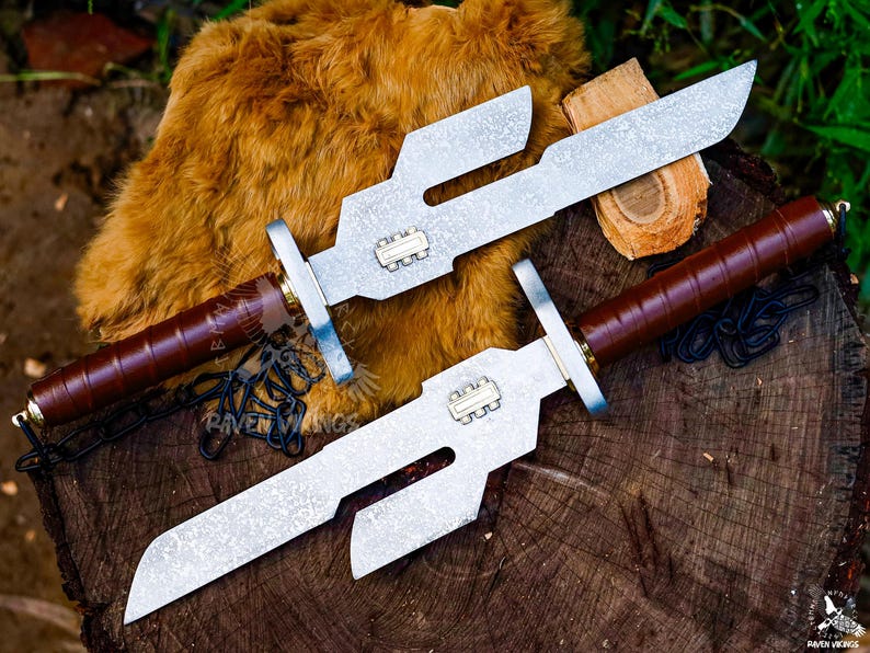 May include: Two custom-made knives with silver blades and brown leather-wrapped handles rest on a wooden surface. The blades have a unique, angular design. The handles are adorned with gold-colored accents. The knives are likely for display or collection.