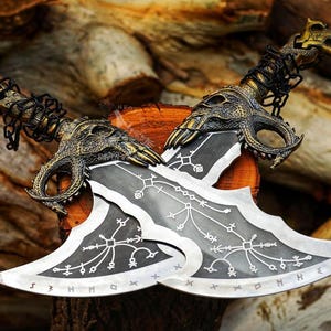 May include: Two silver and black blades with ornate gold and bronze dragon-head handles and chain accents. The blades feature etched designs and are displayed on a wooden surface, showcasing a fantasy theme.