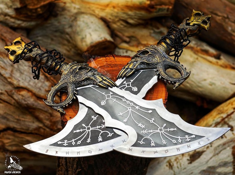 May include: Two silver and black blades with ornate gold and bronze dragon-head handles and chain accents. The blades feature etched designs and are displayed on a wooden surface, showcasing a fantasy theme.
