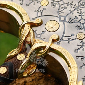 May include: Close-up of a decorative axe head with intricate gold and silver detailing. The axe features a wooden handle wrapped in leather and adorned with gold accents. The blade has etched patterns and gold circular embellishments.