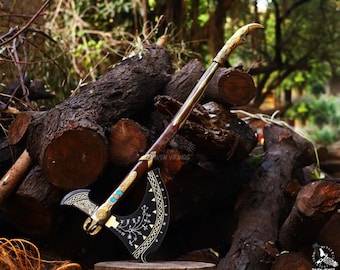 May include: A black and gold axe with a wooden handle and a decorative design. The axe is resting on a pile of logs.