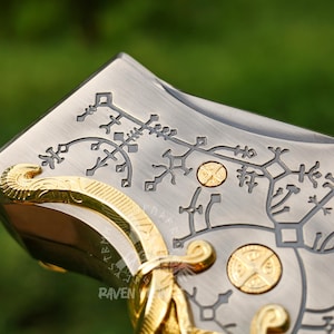 May include: Close-up of a silver and gold metal object with intricate engraved designs. The object features a decorative pattern and gold accents. The Raven Vikings logo is visible in the lower left corner.