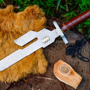 May include: A silver and brown dagger with a textured blade and a leather-wrapped handle. The dagger has a unique, angular design and is accompanied by a black chain. A piece of wood and a fur-like material are also present.
