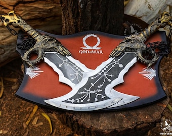 May include: A pair of silver-colored, double-bladed axes with black and gold accents. The axes are mounted on a red and black display board with the words "God of War" printed on it.