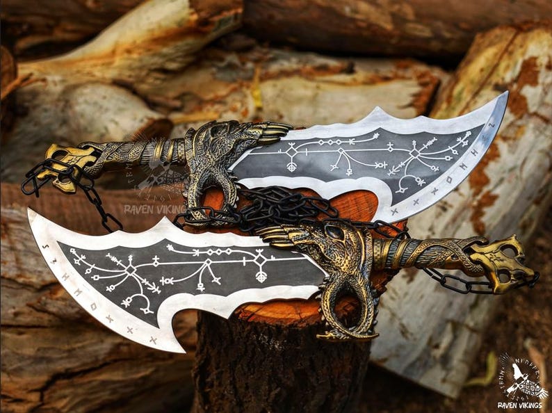 May include: Two silver and black blades with ornate gold handles and chains. The blades have a curved, serrated edge and are decorated with white symbols. The handles feature dragon-like figures. The blades are displayed on a wooden surface.