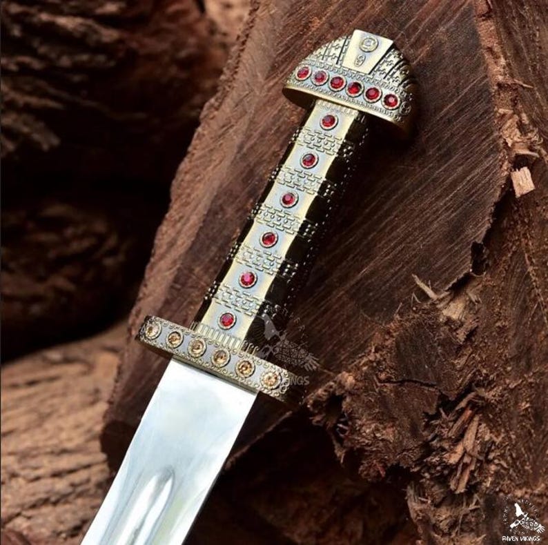 May include: Close-up of a decorative dagger with a silver blade and ornate handle. The handle features gold-colored metal accents and is adorned with red gemstones. The dagger's design suggests a historical or fantasy theme.