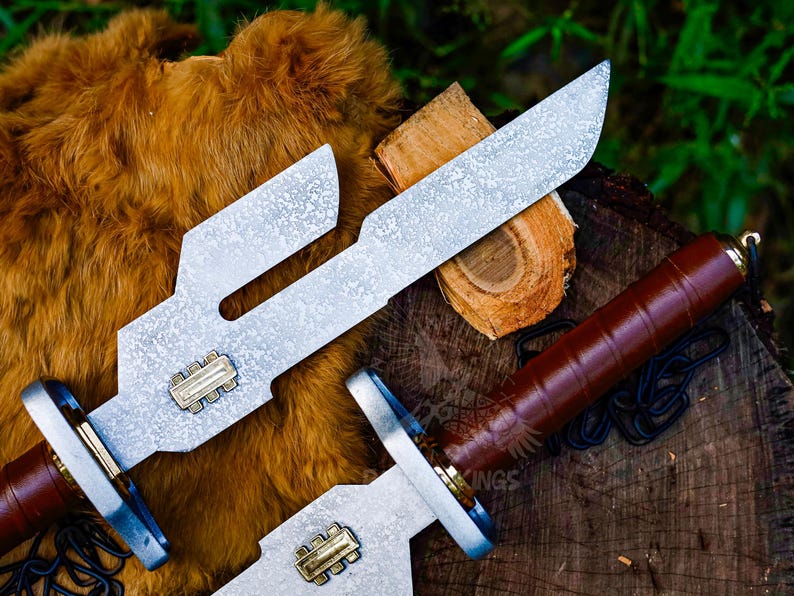 May include: Two silver-colored knives with brown leather handles and a decorative design. The blades have a unique shape with cut-out sections. The handles are wrapped in brown leather. The knives are displayed on a wooden surface with a fur-like background.