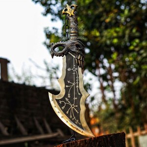 May include: A decorative sword with a black blade and gold accents. The hilt features a dragon design and a chain. The blade has intricate patterns and a curved edge. The sword is displayed on a wooden surface.