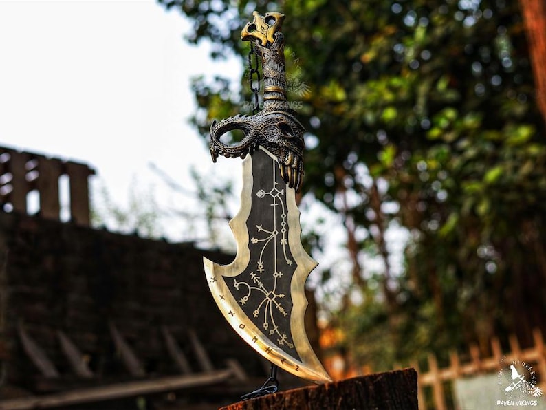 May include: A decorative sword with a black blade and gold accents. The hilt features a dragon design and a chain. The blade has intricate patterns and a curved edge. The sword is displayed on a wooden surface.
