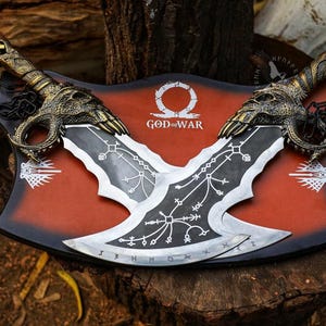 May include: A pair of intricately designed metal blades, featuring ornate handles and a stylized blade design. The blades are mounted on a red and black plaque with the words "God of War". The overall aesthetic is reminiscent of fantasy weaponry.
