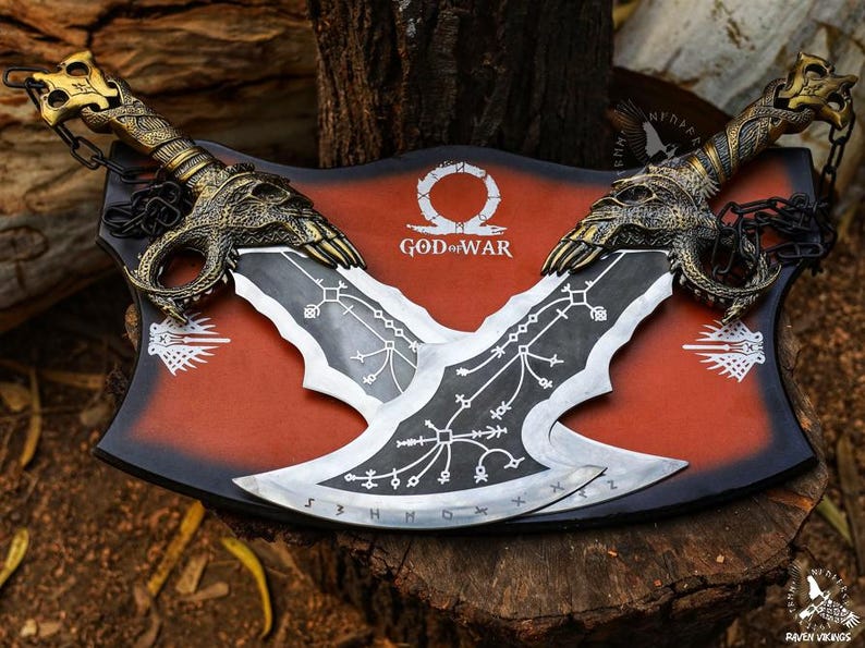 May include: A pair of intricately designed metal blades, featuring ornate handles and a stylized blade design. The blades are mounted on a red and black plaque with the words "God of War". The overall aesthetic is reminiscent of fantasy weaponry.