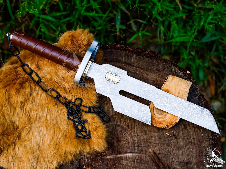 May include: A silver and brown knife with a textured blade and a brown leather-wrapped handle. A black chain is attached to the handle. The knife is resting on a wooden surface with a brown fur-like material.