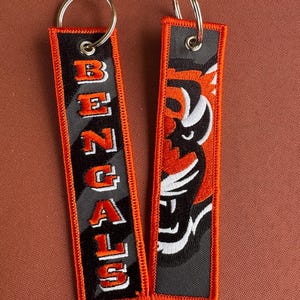 May include: Two rectangular keychains with metal rings. One features the word "BENGALS" in orange and white on a black and gray background. The other displays a tiger head design in orange, black, and white.