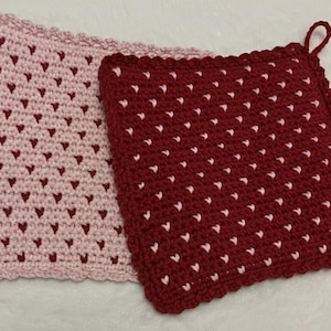 Puede incluir: Dos agarraderas de ganchillo hechas a mano. Una es rosa claro con corazones rosa oscuro, la otra es burdeos con corazones blancos. La agarradera burdeos tiene un lazo para colgar. Ambas son cuadradas y tienen un borde festoneado.