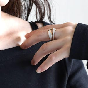 Peut inclure: Une bague en or avec un motif en émail blanc. La bague est en forme de deux lignes ondulées qui s'entremêlent.