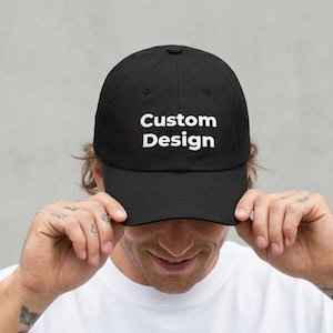 Puede incluir: Una gorra de béisbol negra con el texto blanco Custom Design centrado en el panel frontal. La gorra tiene una corona estructurada, una visera curva y un botón en la parte superior. El diseño es sencillo y resalta las letras blancas con claridad.