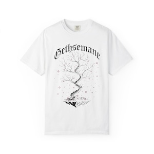 May include: White t-shirt featuring a black and white illustration of a tree with the word "Gethsemane" above it. The tree is on a floating island with small pink star-shaped accents.