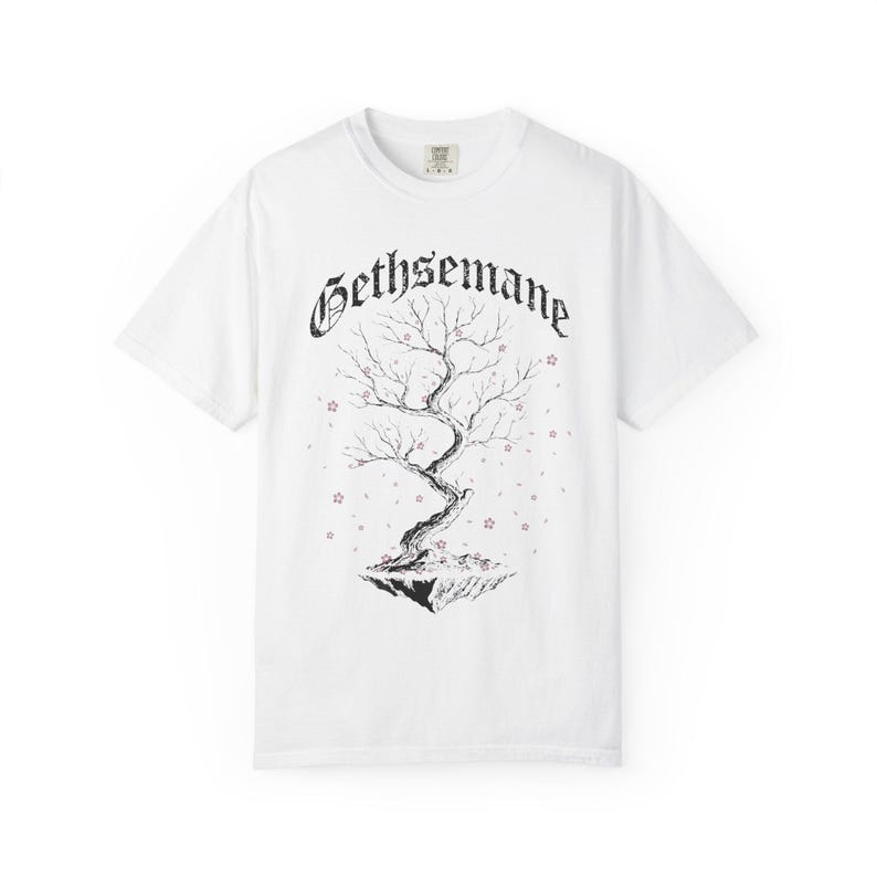 May include: White t-shirt featuring a black and white illustration of a tree with the word "Gethsemane" above it. The tree is on a floating island with small pink star-shaped accents.