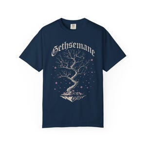 May include: Navy blue t-shirt featuring a tree graphic with the word "Gethsemane" above it. The tree has bare branches and pink blossoms. The design is centered on the shirt.