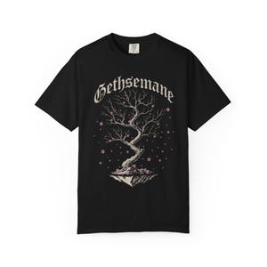 May include: Black t-shirt featuring a stylized tree design with the word "Gethsemane" in an ornate font. The tree has delicate branches and pink blossoms, with some falling around it. The design is centered on the shirt.