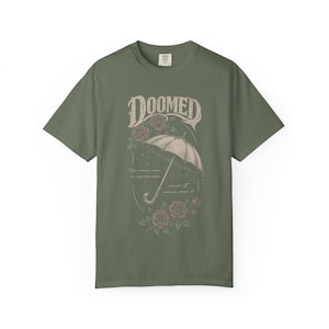 moss color Comfort Colors T-shirt featuring a vintage gothic umbrella illustration with roses and rain details and the word “Doomed” in distressed lettering.